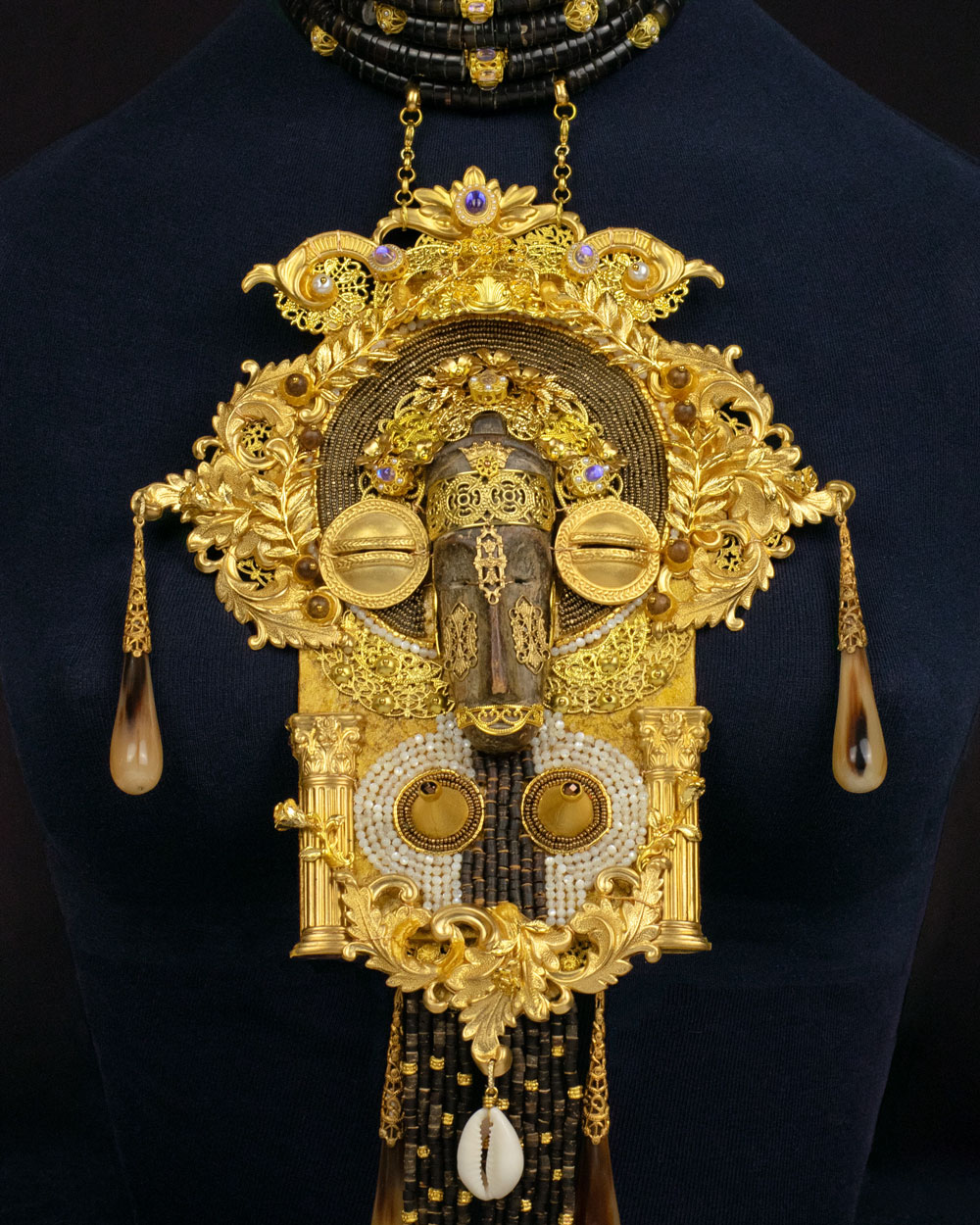Detail of hand-carved African wooden mask pendant with brass filigree, cowrie shells and freshwater pearls, Lacrimae Mundi collection